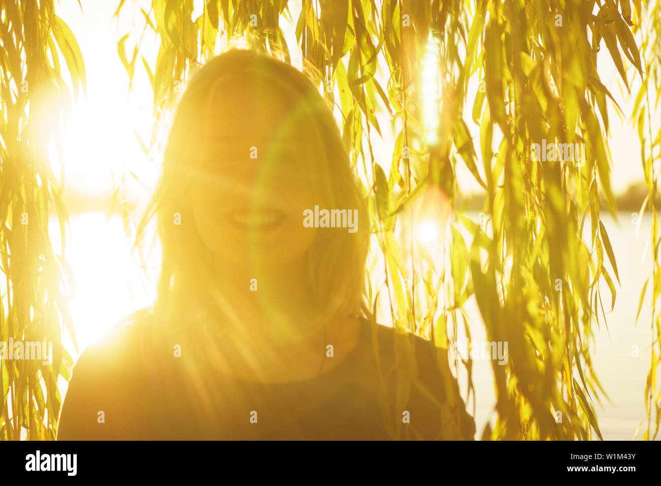 Autunno Ritratto di giovane sorridenti ragazza bionda con battenti capelli con i rami di salici sullo sfondo di un lago al tramonto Foto Stock