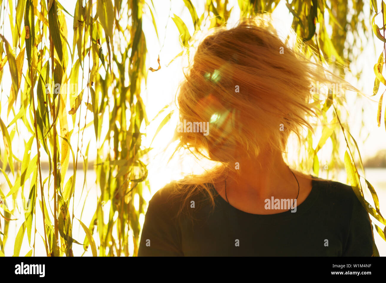 Autunno Ritratto di giovane sorridenti ragazza bionda con battenti capelli con i rami di salici sullo sfondo di un lago al tramonto Foto Stock