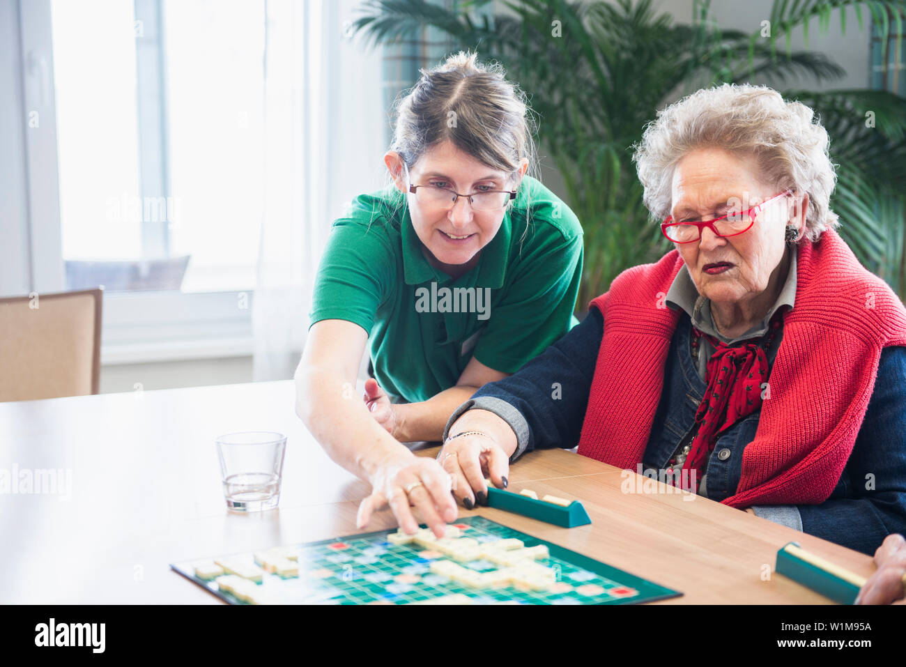 Il personale infermieristico che assiste il senior donna giocare a scrabble gioco di bordo Foto Stock
