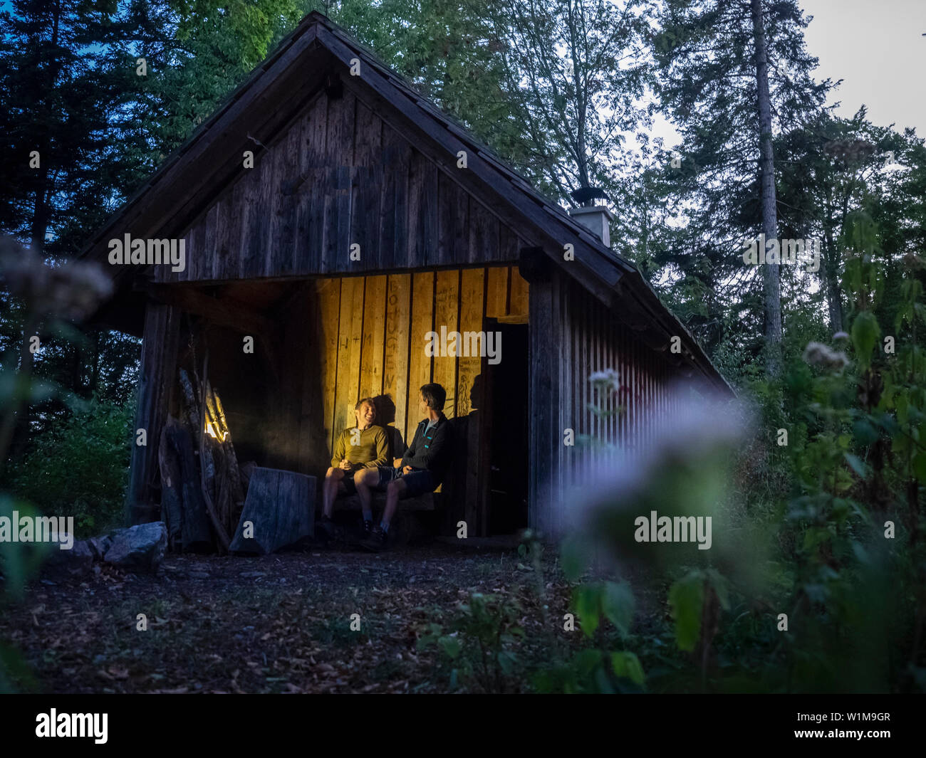 Due escursionisti maschio rilassarsi di fronte della piccola capanna nella Foresta Nera di notte, Baden-Württemerg, Germania Foto Stock