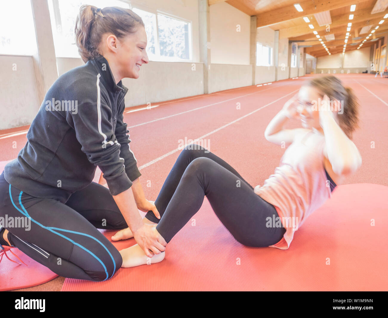 Istruttore di Fitness aiutando giovane donna facendo sit ups in sala di atletica sulla pista di tartan, Offenburg, Baden-Württemberg, Germania Foto Stock