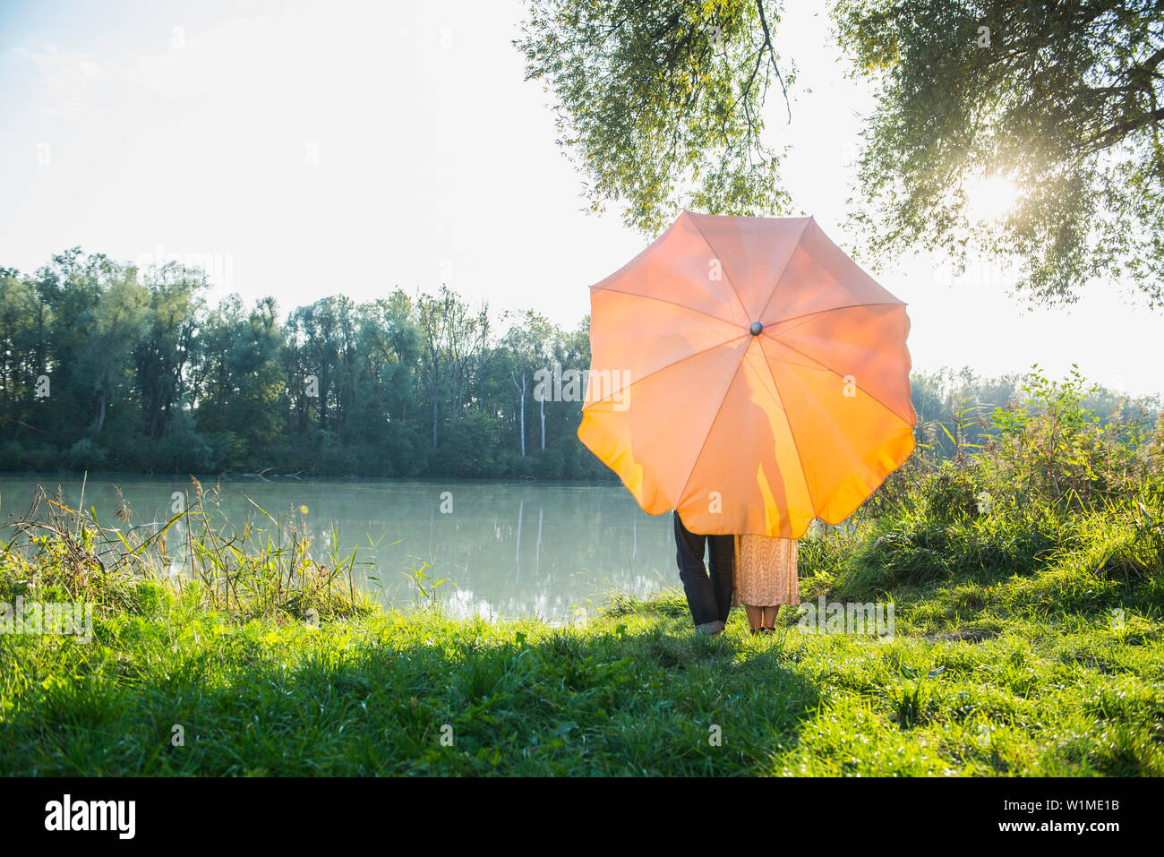 Matura in piedi dietro a ombrellone a riverbank contro la luce solare, Baviera, Germania Foto Stock