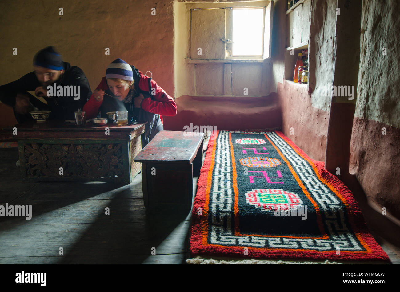 Il giovane e la giovane donna di mangiare in un tipico tibetano stanza vivente, casa in Lupra, piccolo villaggio con un Gompa buddista alla Kali Gandaki valley, Foto Stock