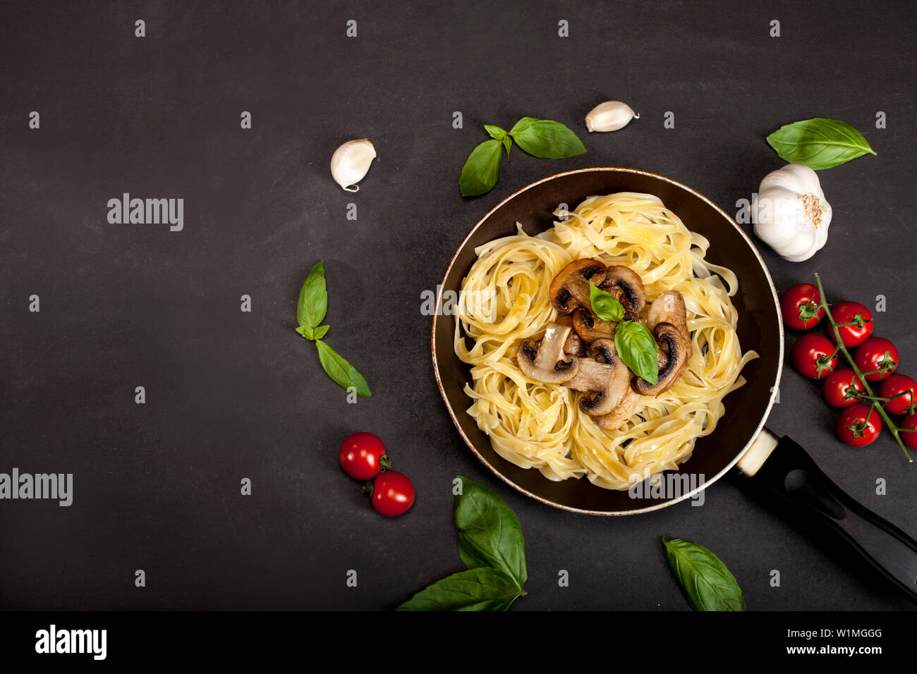 Tagliatelle con funghi freschi e basilico in una padella su sfondo nero con copia spazio. Vista dall'alto. Foto Stock