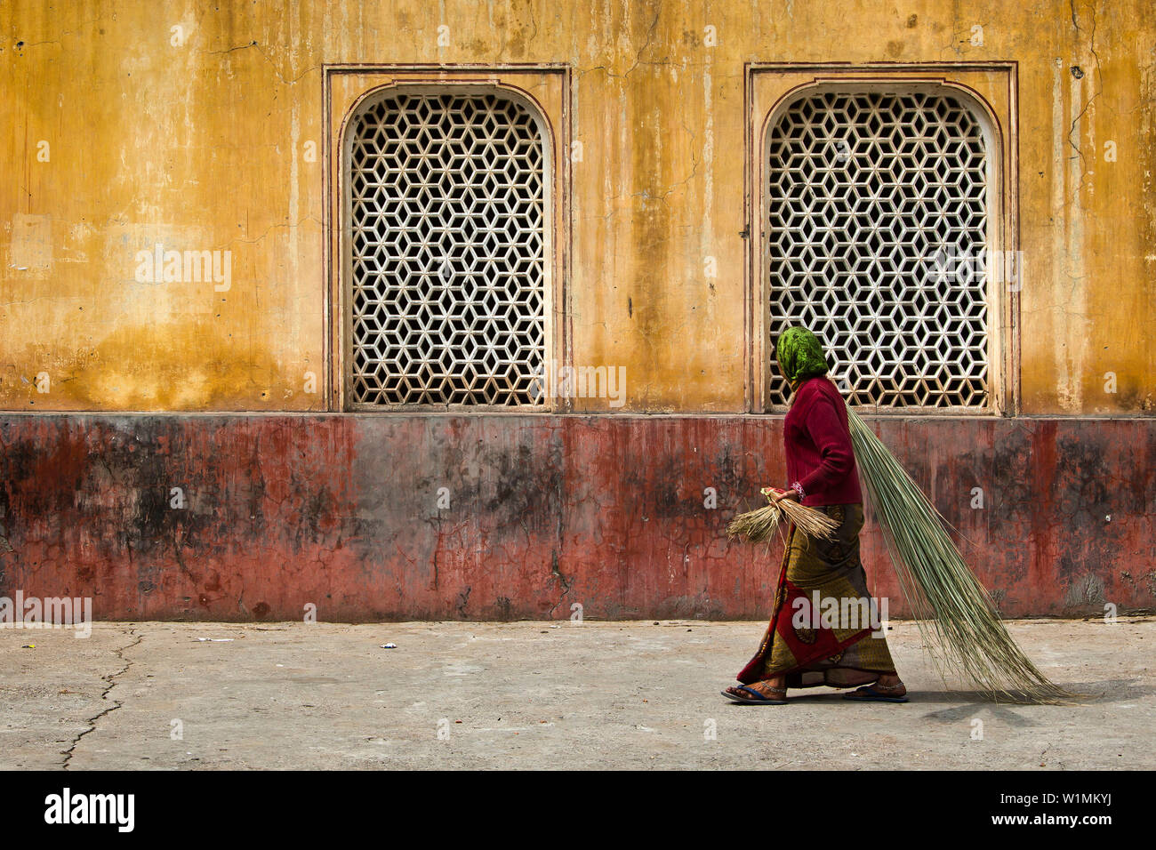 Donna con spazzole di bambù di fronte ad un edificio nel tempio Galtaji, Jaipur, Rajasthan, India Foto Stock