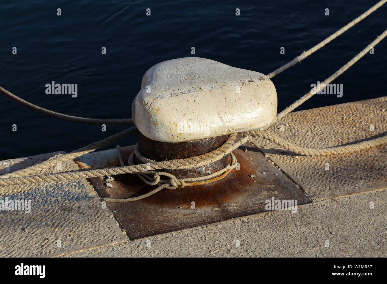 Bollard con una linea di ormeggio avvolto intorno ad esso. Barche ormeggiate presso il porto degli yacht. Foto Stock