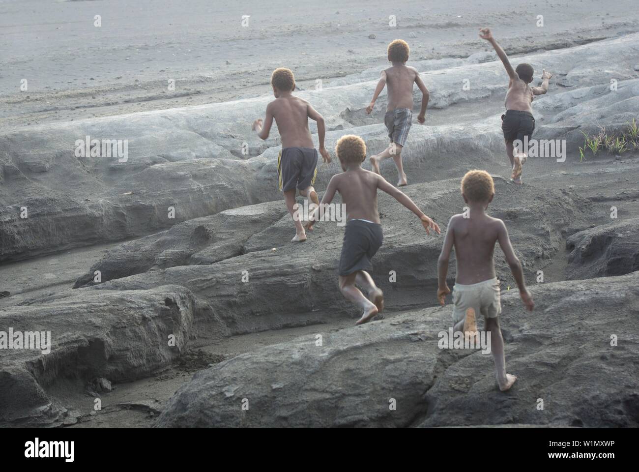 Bambini che giocano e corrono attraverso il campo di cenere ai piedi del vulcano Tavurvur, Papua Nuova Guinea, Nuova Gran Bretagna, Sud Pacifico Foto Stock