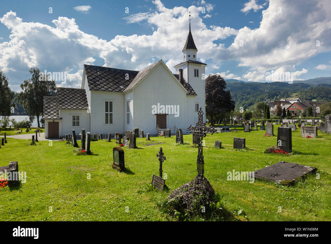 Chiesa di Ulvik con cielo blu, di fiori e di tombe in estate, Hardangerfjord, Hordaland, Norvegia e Scandinavia Foto Stock