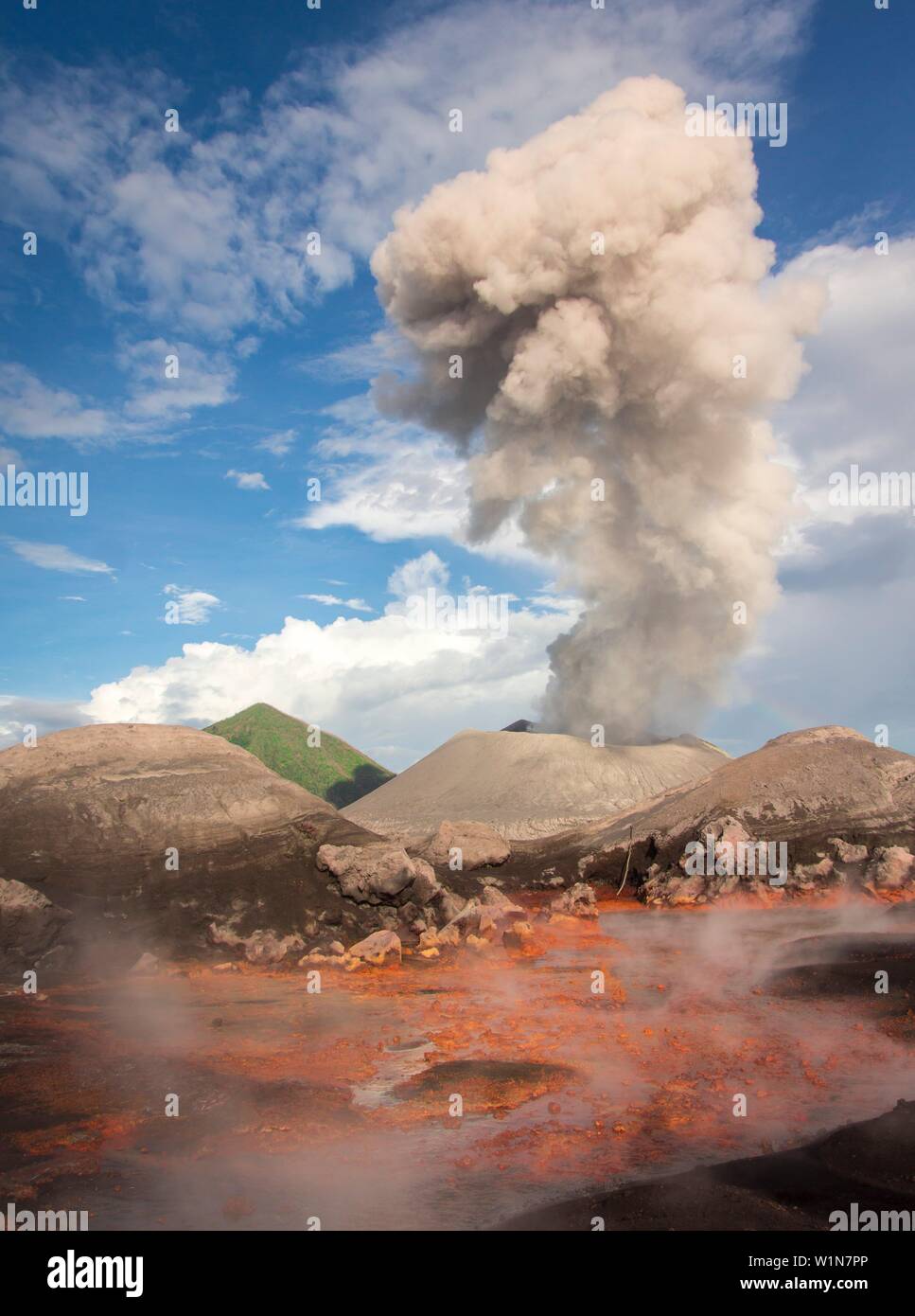 Eruzione del vulcano attivo Tavurvur con la nube di cenere e vapore caldo di molle di zolfo nella parte anteriore; verde cono del ''Vulcan'' vulcano nel retro, Pa Foto Stock