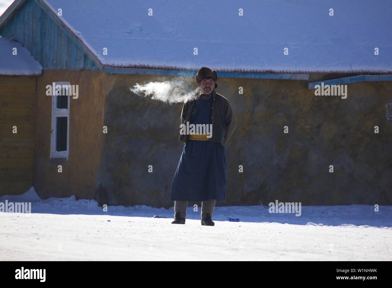 Uomo mongolo di fumare nella tradizionale Deel, Mongolia Foto Stock