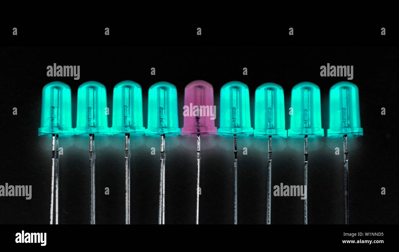 Essere diversi e stare fuori dalla folla del concetto: un LED viola tra otto quelli ciano. Sfondo nero e spazio copia 16:9 Foto Stock