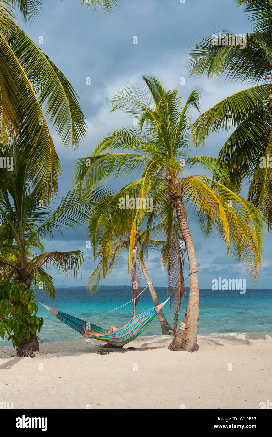 Un visitatore giornaliero da una spedizione nave da crociera si rilassa in una amaca appesa tra palme sulla spiaggia, isole San Blas, Panama, dei Caraibi Foto Stock