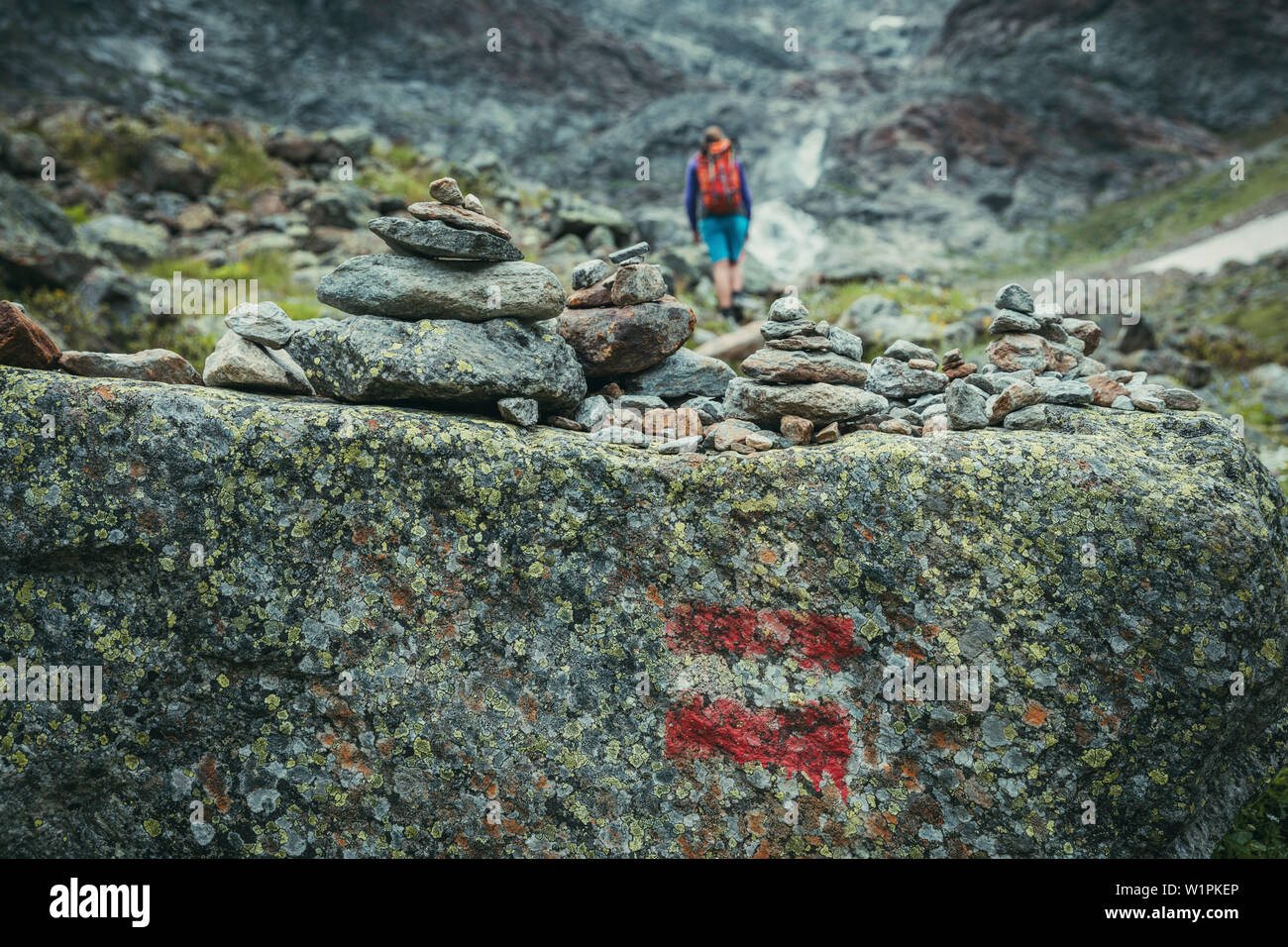 Blocchi di pietra con il marcatore di orientamento e alpinista in background, E5, Alpenüberquerung, quarto stadio, Skihütte Zams,Pitztal,Lacheralm, Wenns, Gletsche Foto Stock