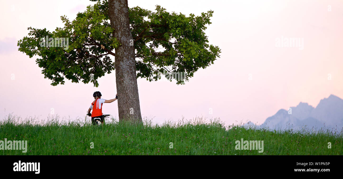 Ragazza seduta sulla sua bicicletta e tenuta su di un albero, Fuessen, Baviera, Germania Foto Stock