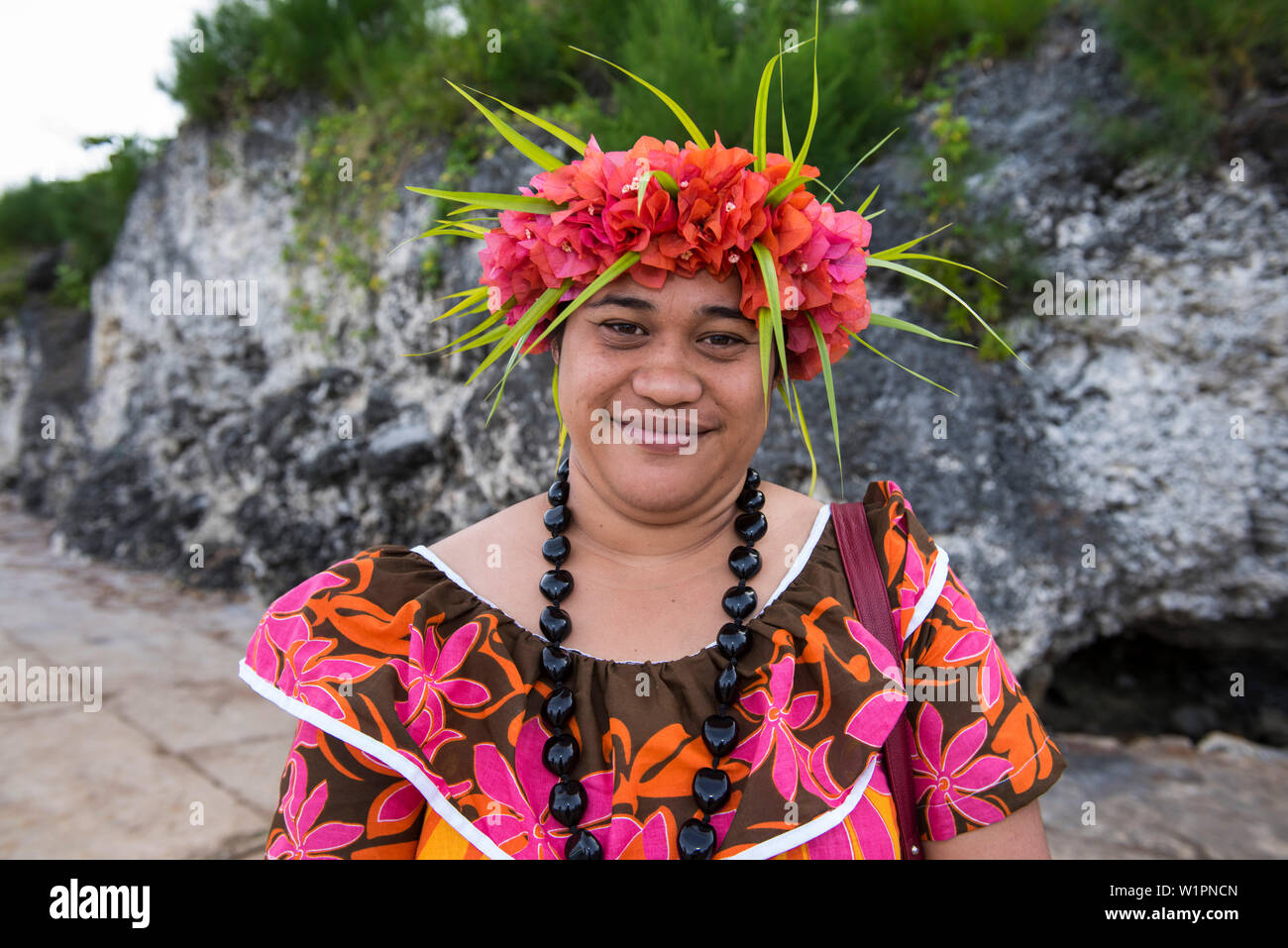 Una donna locale indossando un vivacemente colorato di fiori abito di stampa, una collana fatta di semi di grandi dimensioni e un copricapo di fiori e foglie sorrisi nella camma Foto Stock