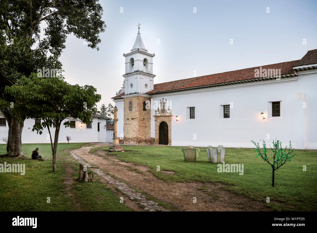 Indigenious donna seduta davanti della cattolica chiesa Iglesia del Carmen in città storica Villa de Leyva, Departamento Boyacá, Colombia, Sud America Foto Stock