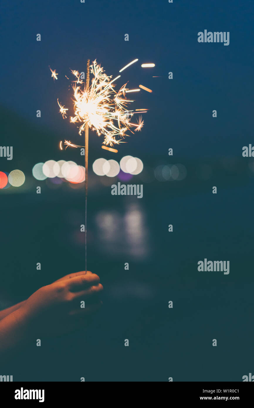 Il Bengala fire sparkler in mano all'aperto in serata su uno sfondo bokeh luci della città, il concetto di Natale. Foto Stock