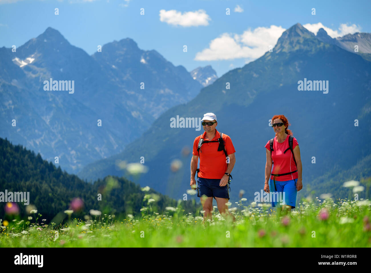 L uomo e la donna escursionismo su Lechweg attraverso il prato con fiori, Lechtal Alpi in background, Weissenbach, Lechweg e la Valle del Lech, Tirolo, Austria Foto Stock