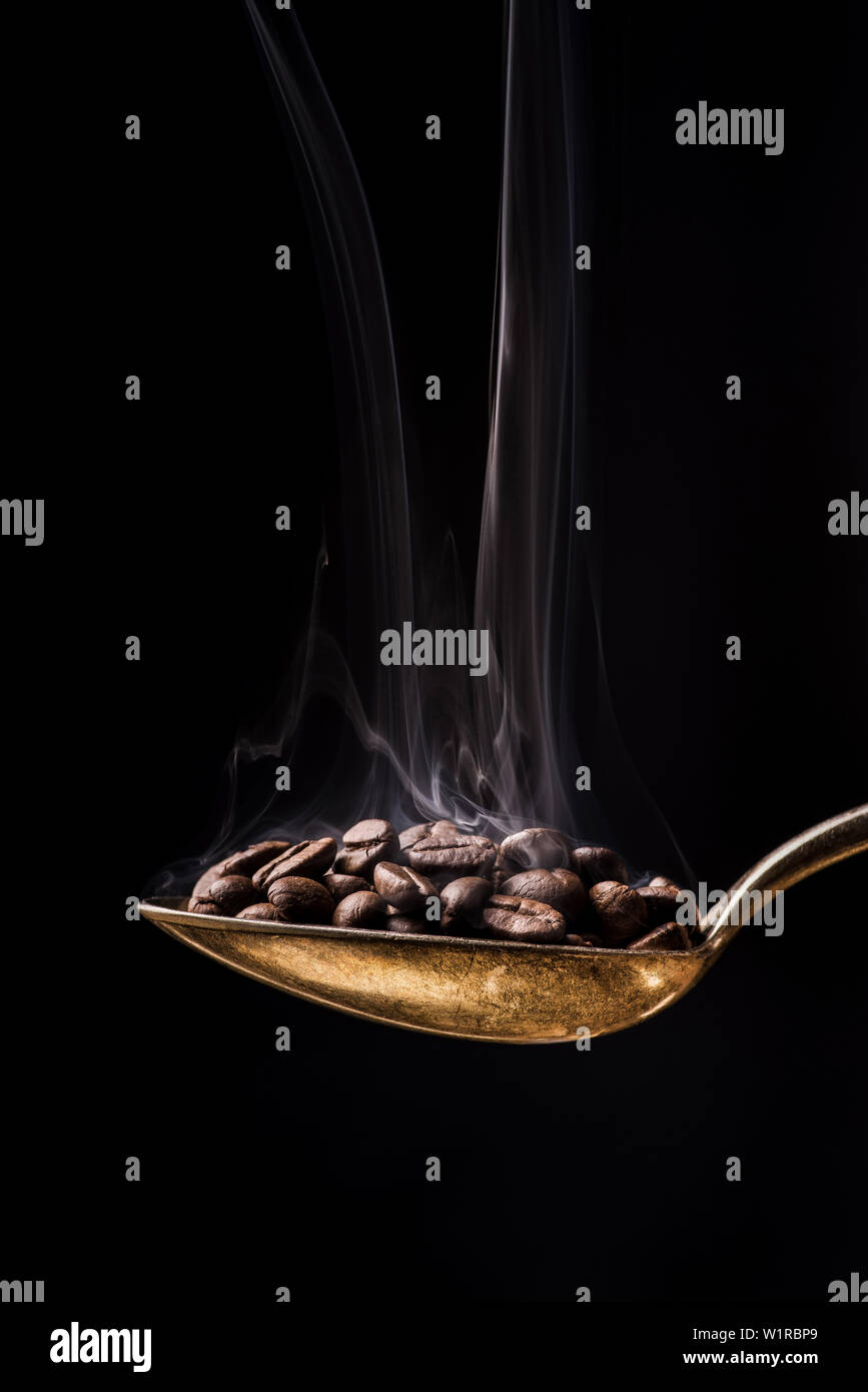 Close-up di un cucchiaio a caffè torrefatto in grani aromatizzato caldo contro lo sfondo scuro Foto Stock