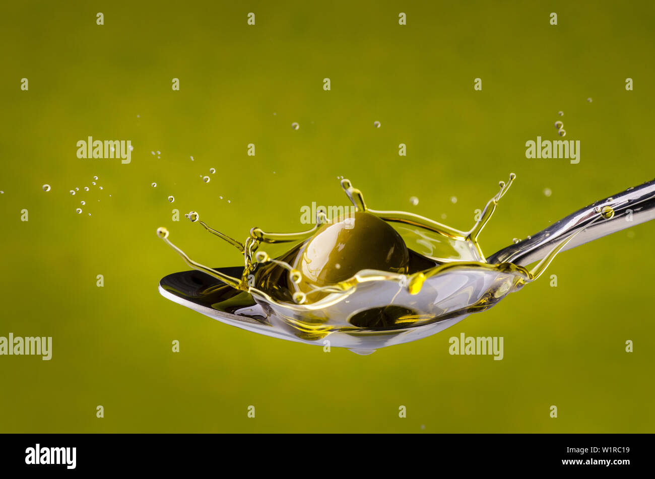 Schizzo con goccioline ottenute da un'oliva che cade in un cucchiaio di olio di oliva extra vergine Foto Stock