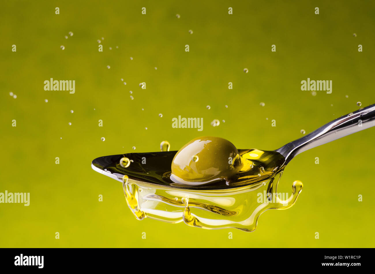 Schizzo con goccioline ottenute da un'oliva che cade in un cucchiaio di olio di oliva extra vergine Foto Stock