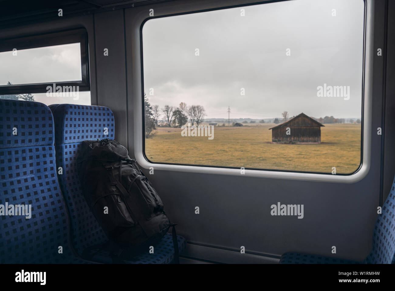 Treno tedesco interno con uno zaino nero sulla sedia blu e una casetta di legno visualizzati sulla finestra del treno. Autunno del concetto di viaggio. Foto Stock