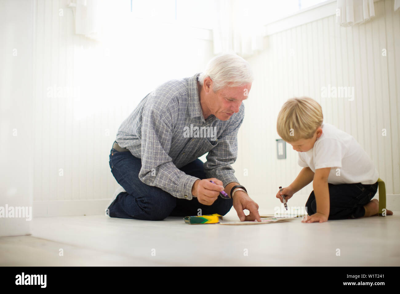 Nonno e nipote di Disegno con matite colorate mentre inginocchiati sul pavimento. Foto Stock