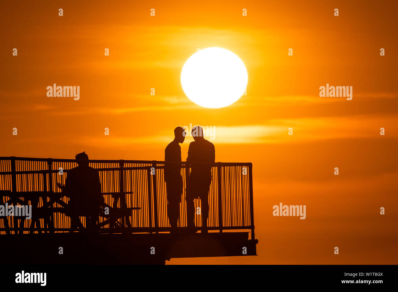 Aberystwyth Wales UK, mercoledì 03 luglio 2019 UK Meteo: persone in piedi alla fine di Aberystwyth troncato del molo sul mare si stagliano contro il cielo come si guarda il glorioso tramonto su Cardigan Bay sulla costa del Galles occidentale. Photo credit: Keith Morris/Alamy Live News Foto Stock