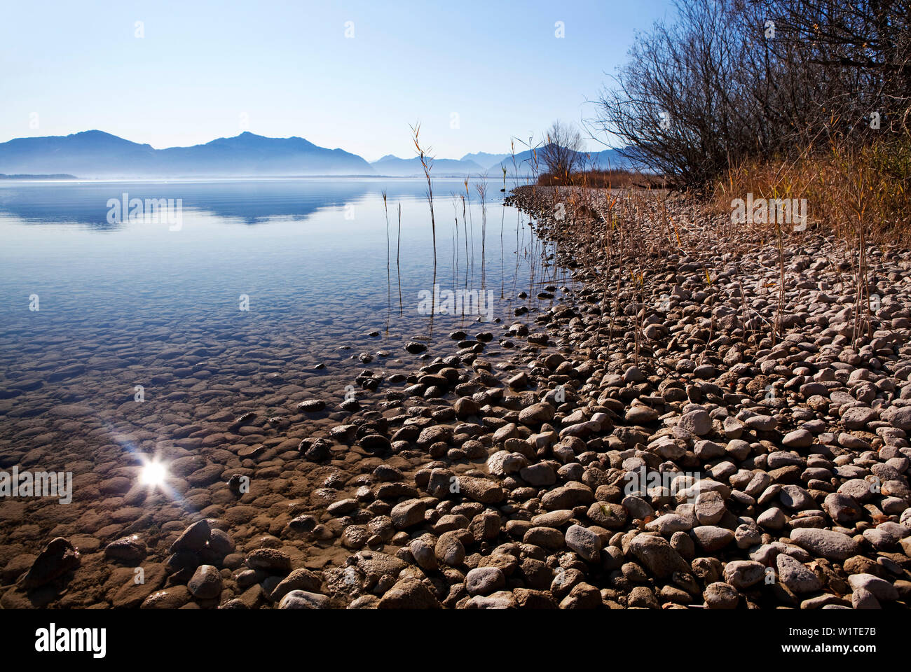 Fondale basso accanto a una banca di ghiaia nel lago Chiemsee e le montagne di Chiemgau in background Foto Stock