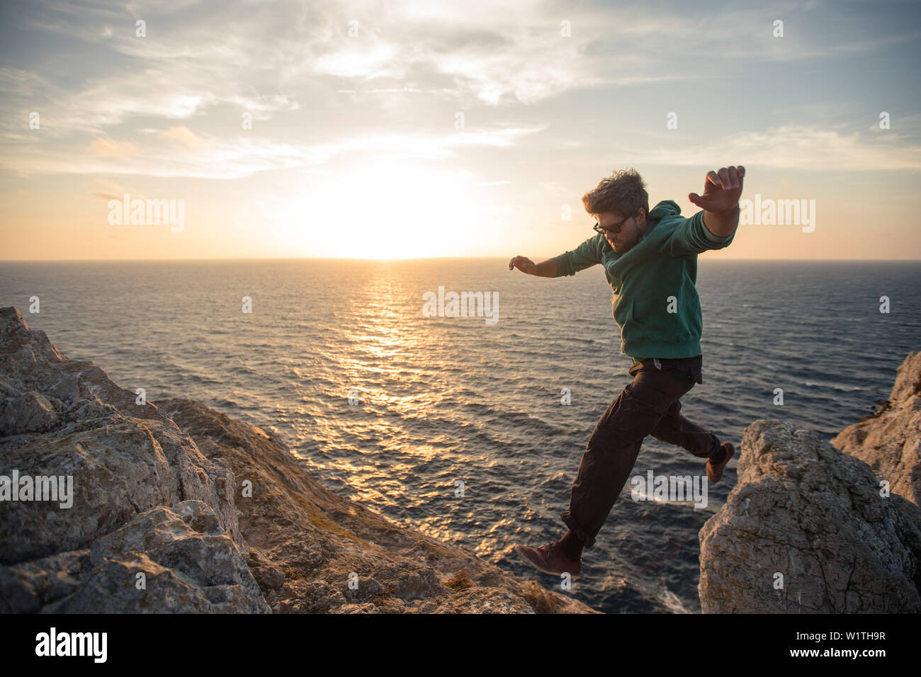 Giovane uomo saltando su una scogliera alla spiaggia Praia da Amoreira, Aljezur, Faro, Portogallo Foto Stock