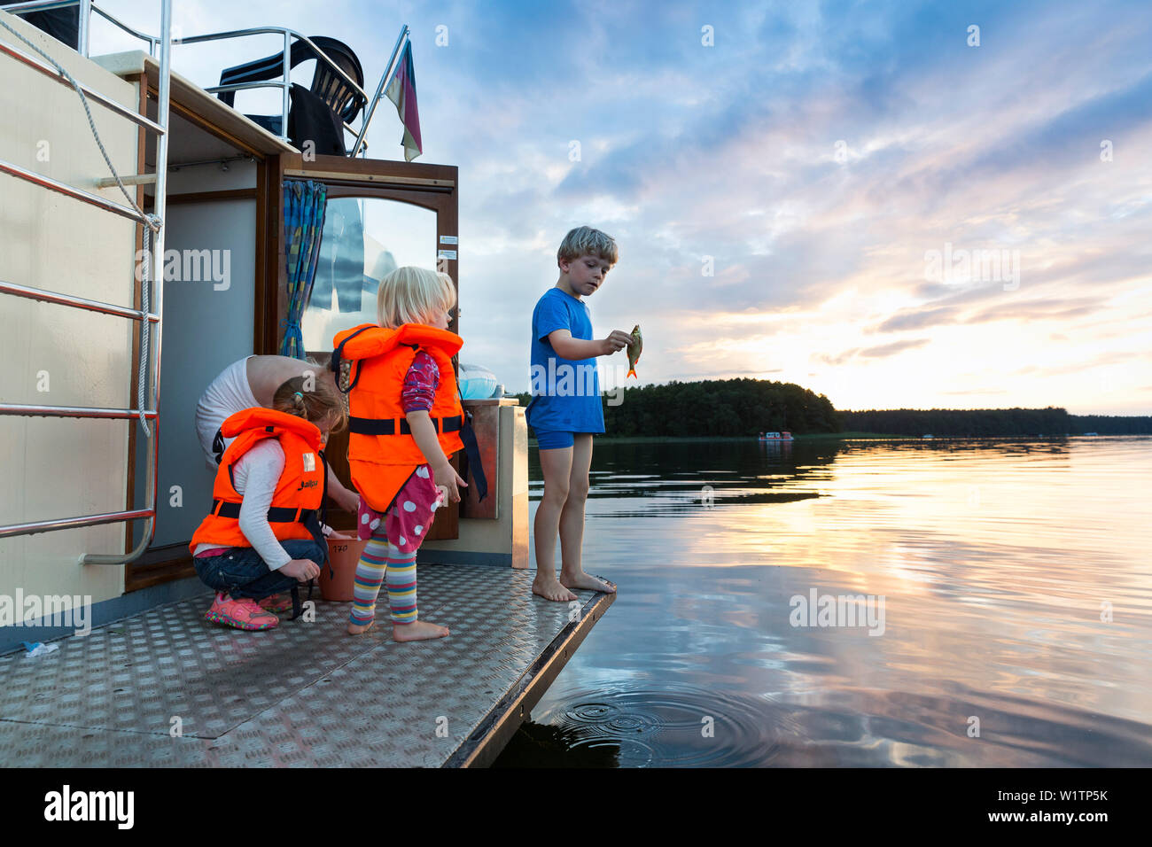I bambini la pesca su una barca, tramonto, houseboat tour, Zotzensee lago, vicino al lago di Müritz, Kuhnle-Tours, Mecklenburg laghi, Meclemburgo Lake District, Signor, Foto Stock