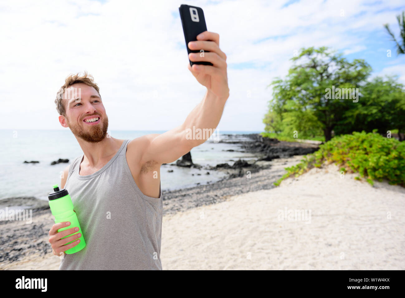 Uomo Fitness tenendo selfie di se stesso dopo l'allenamento. Buona ricerca giovane adulto prendendo un autoritratto foto con la sua fotocamera dello smartphone dopo aver esercitato su una spiaggia durante le vacanze estive in viaggio. Foto Stock