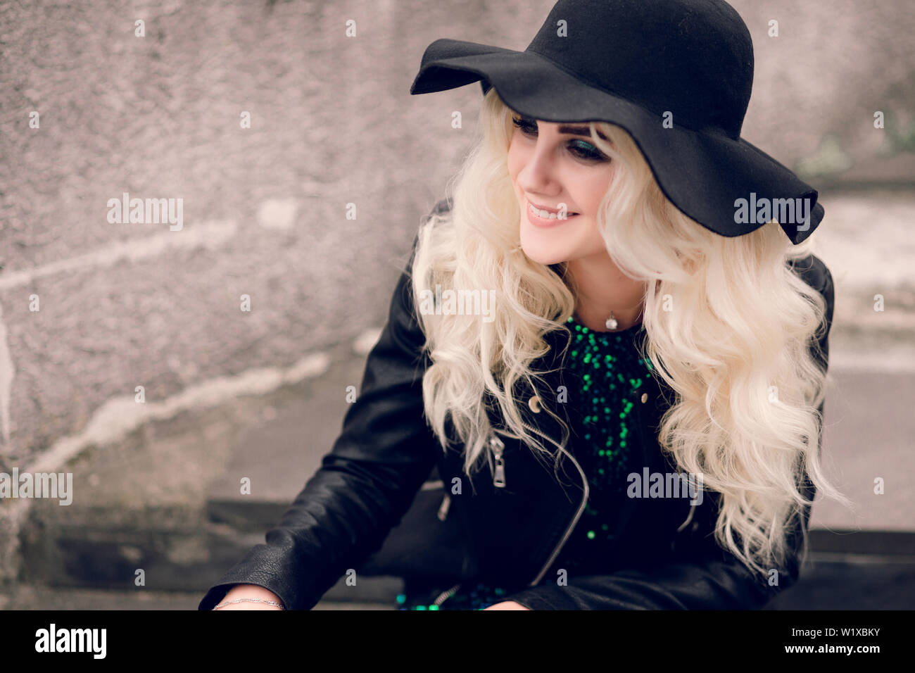La ragazza nel cappello nero e giacca di pelle si siede e sorrisi Foto  stock - Alamy