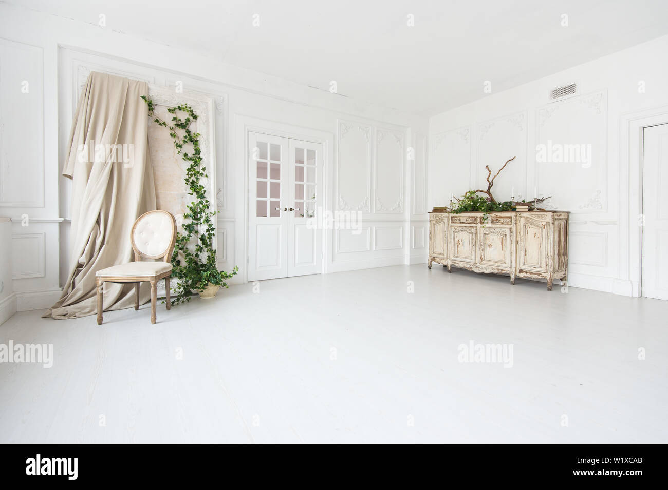 Luce di lusso interno della camera con lo stucco sulle pareti, vintage sedia, e cassettiera decorata con piante. Foto Stock
