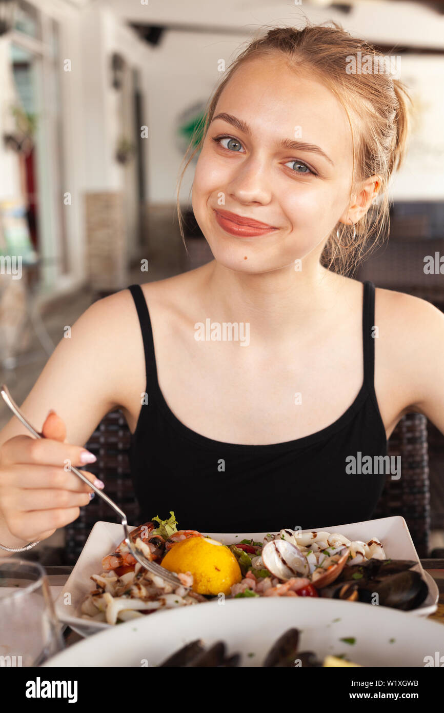 Sorridente bella bionda ragazza caucasica mangia insalate di pesce in un ristorante mediterraneo Foto Stock