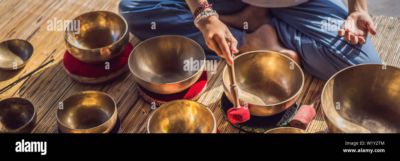 Donna che gioca su Tibetan Singing Bowl mentre è seduto sul materassino yoga contro una cascata. Tonned vintage. Bellissima ragazza con perle di mala meditando BANNER Foto Stock