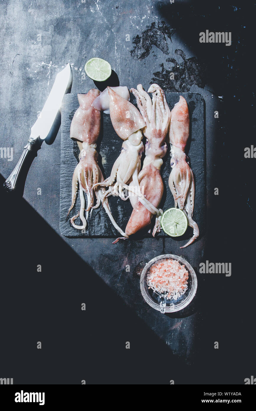 Calamari,piatti di pesce calamari, su uno sfondo nero,ancora la vita, vista dall'alto con luce naturale, tono scuro. Foto Stock