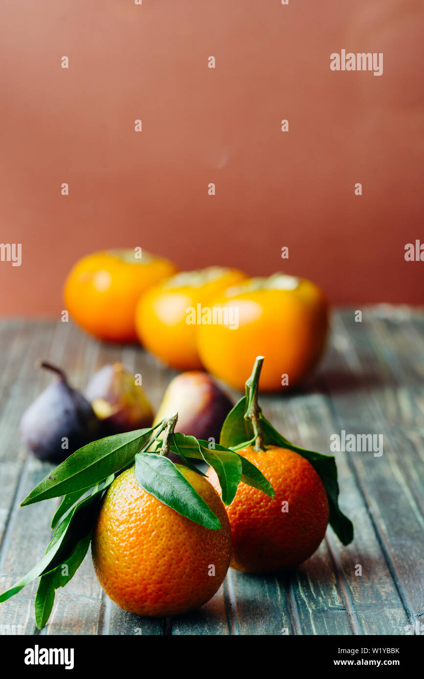 Mandarino Satsuma con foglie su un tavolo in legno con fichi freschi tonalità scura, Foto Stock