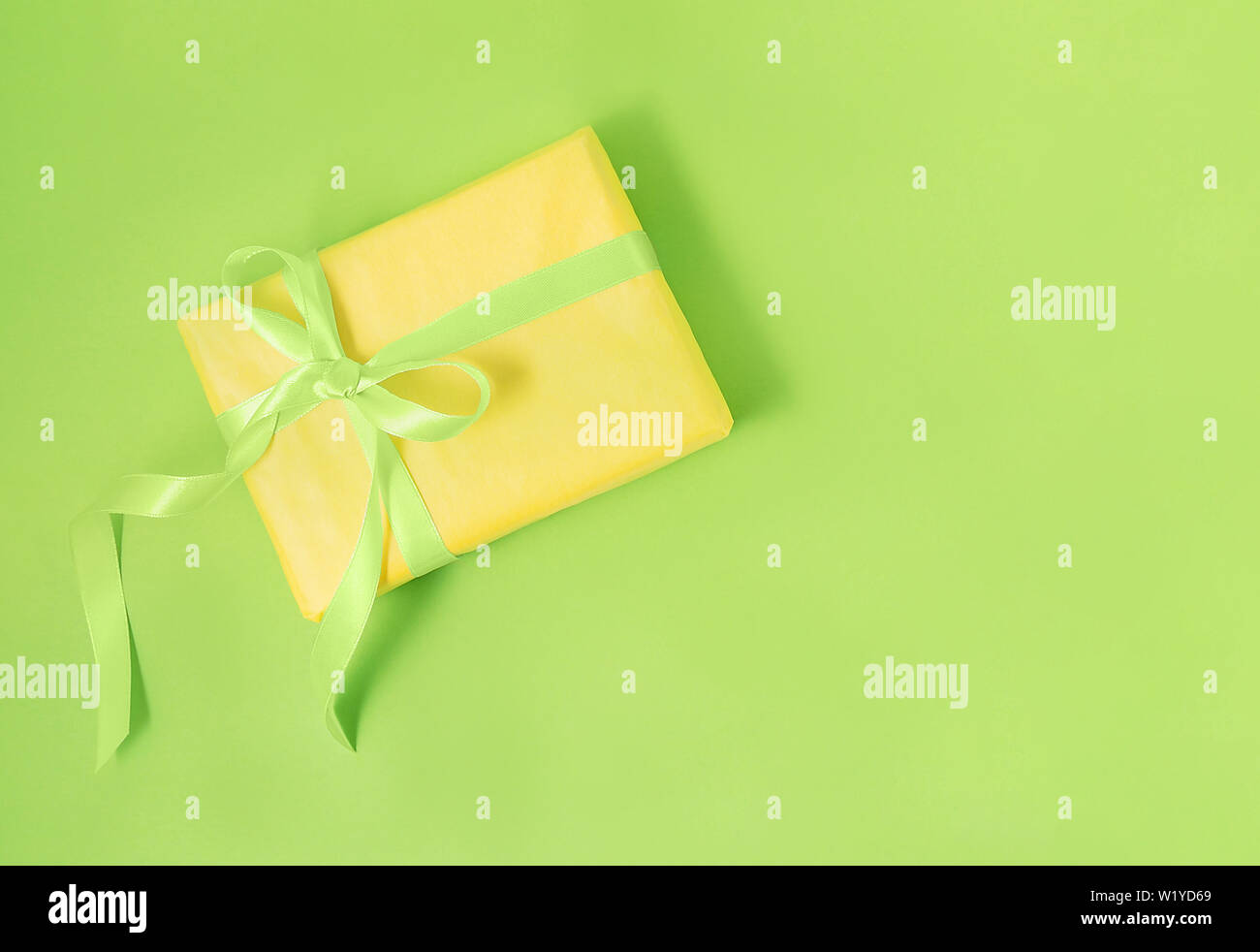Giallo confezione regalo con seta verde nastro pastello su sfondo verde. Holiday Gift concept. Lay piatto. Copia dello spazio. Foto Stock