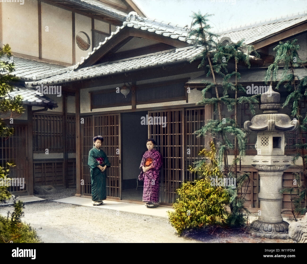 [ 1930 Giappone - ingresso di una casa Giapponese ] - due donne in kimono stand all'ingresso, chiamato genkan, di una casa di quello che sembra essere un bene-a-fare famiglia. Vi è un enorme lanterna di pietra e la grande area aperta di fronte all'ingresso suggerisce molto spazio tra l'ingresso e la porta. Xx secolo vintage vetrino di vetro. Foto Stock