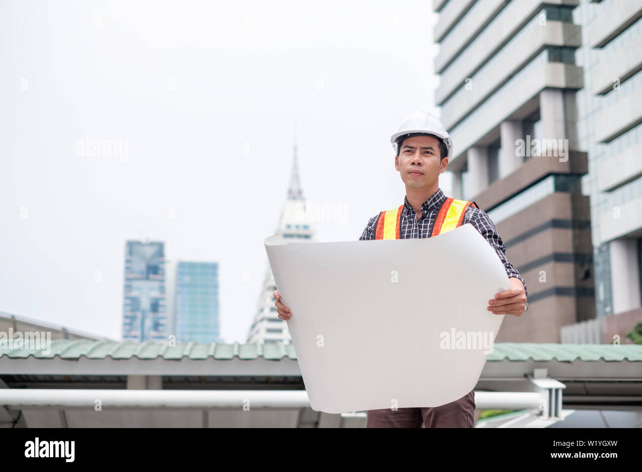 Ingegnere Man Standing open blueprint con cercando essere concentrati nella città Foto Stock