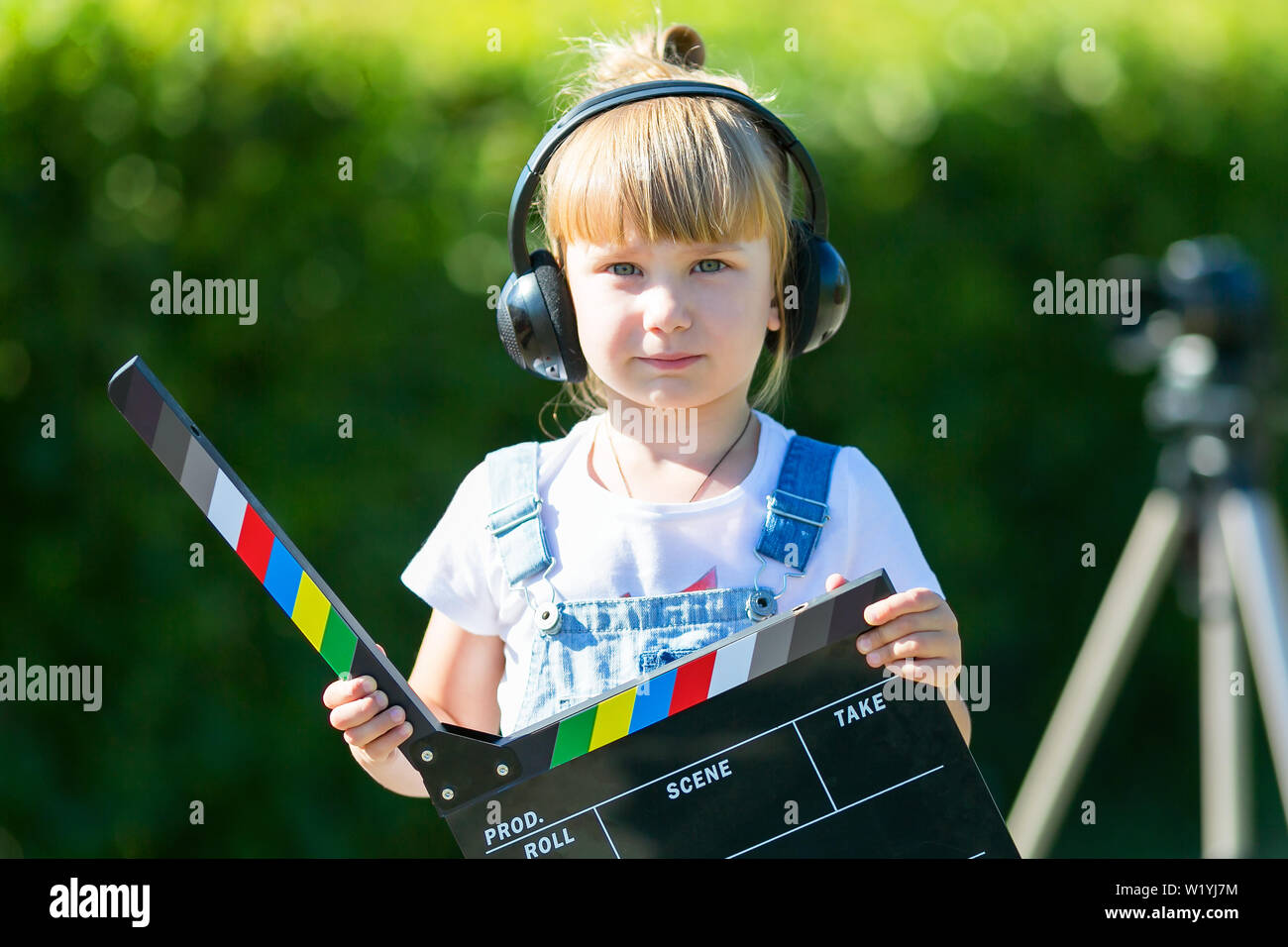 Bambina con le cuffie con un TV numeratore nelle sue mani è in piedi accanto alla videocamera su un treppiede. Foto Stock