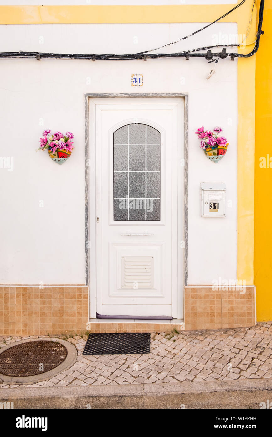 Sportello anteriore al grazioso e bianco verniciato giallo-house con cesti di fiori in Alvor, Algarve, PORTOGALLO Foto Stock