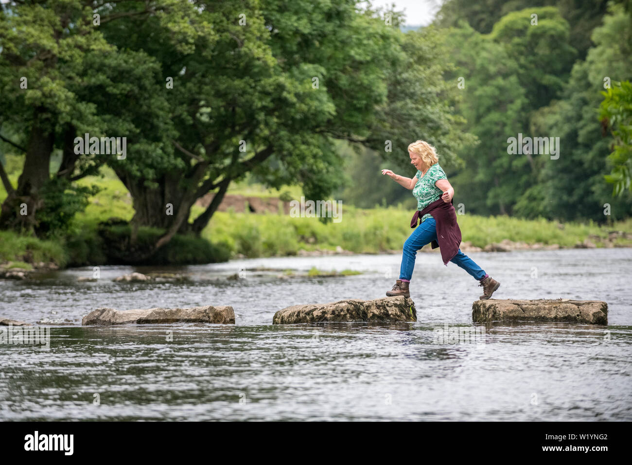 Walker per le pietre miliari che attraversa il Fiume Ure a Redmire, Yorkshire Dales, UK. Foto Stock