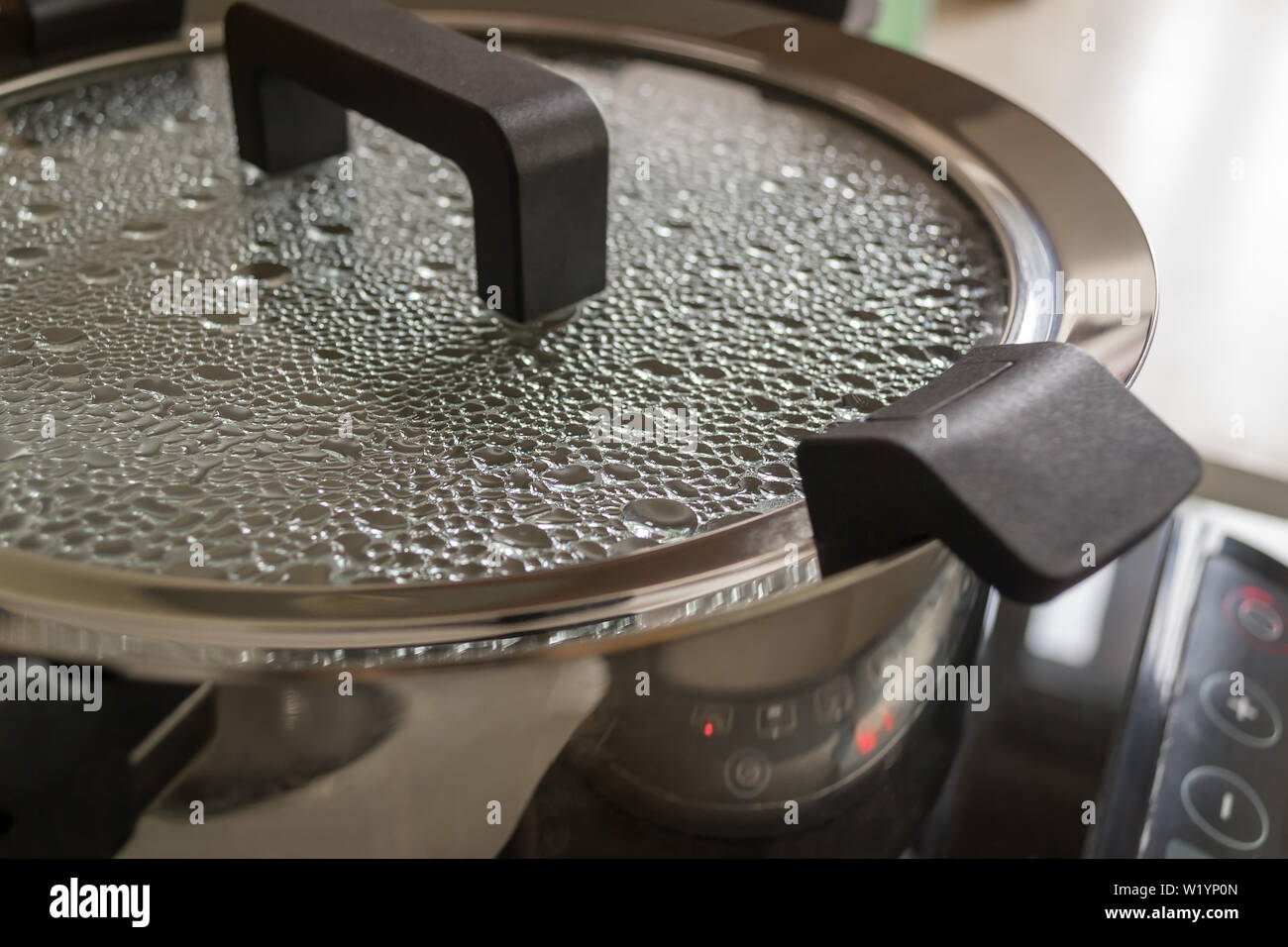 Metallo moderno zuppa di pentola o padella con maniglie nere su un fornello  ad induzione. Gocce di acqua bollente sono sulla superficie interna del  vetro trasparente coperchio Foto stock - Alamy