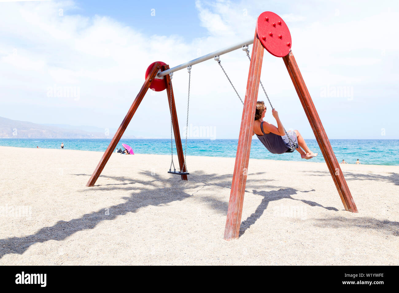 Donna di mezza età basculante in una oscillazione. Sulla spiaggia con il sole sulla sua faccia in Spagna. Foto Stock