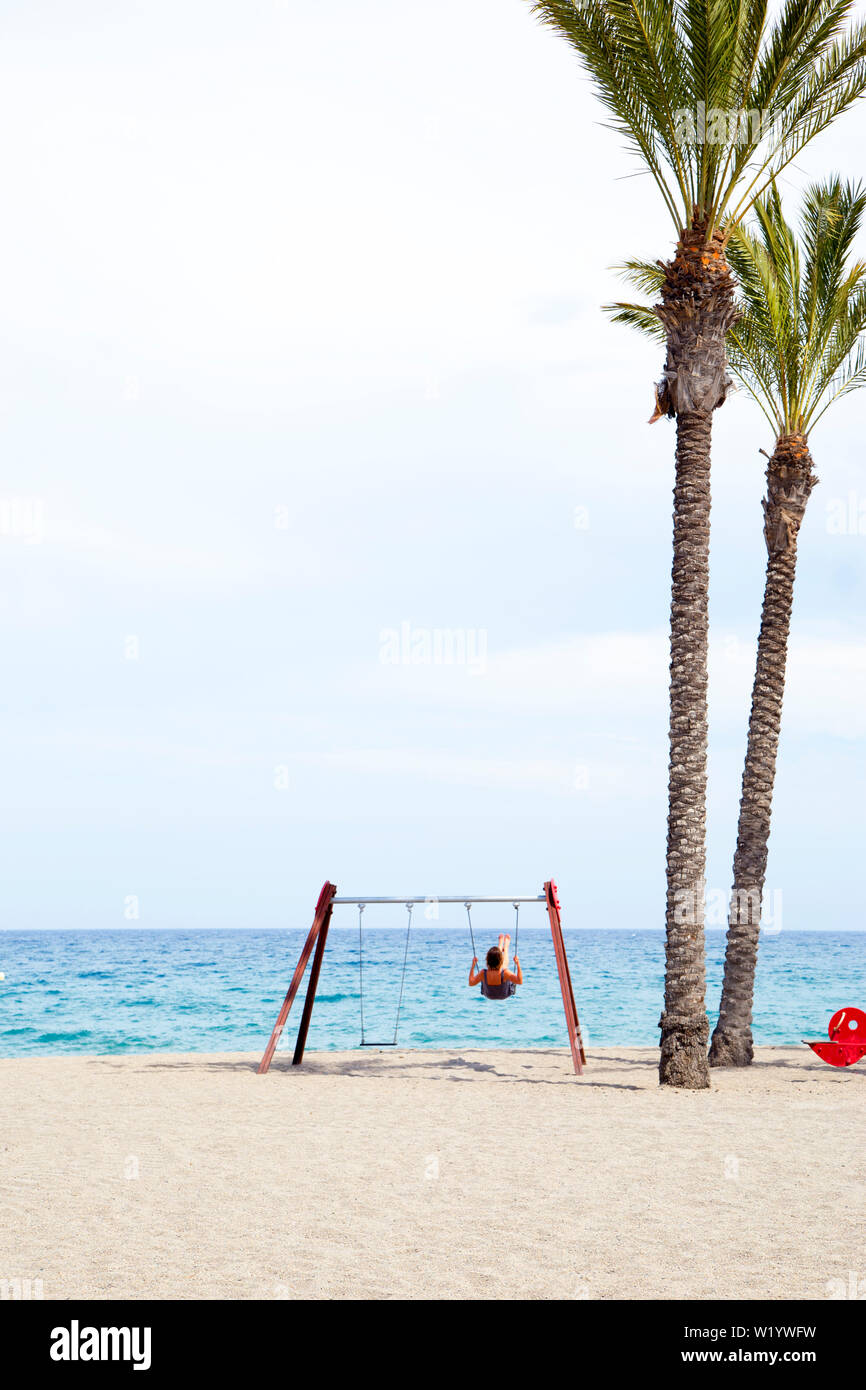 Donna di mezza età basculante in una oscillazione. Sulla spiaggia con il sole sul suo viso. Foto Stock