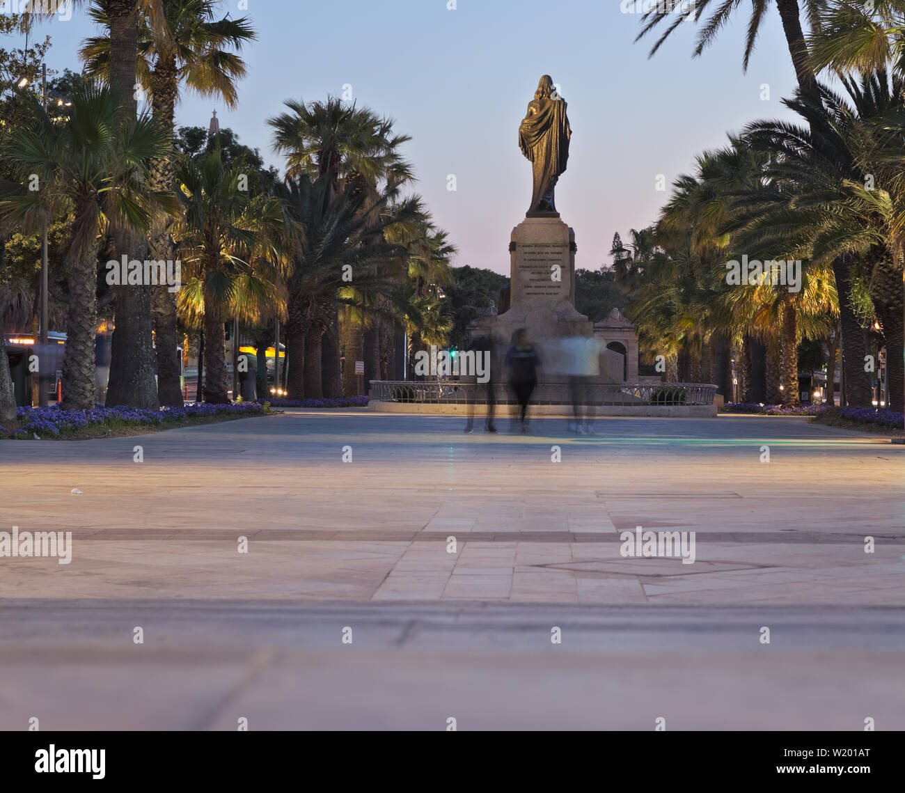 La gente che camminava davanti a Cristo re statua al tramonto accanto alla famosa fontana del Tritone a La Valletta. Foto Stock