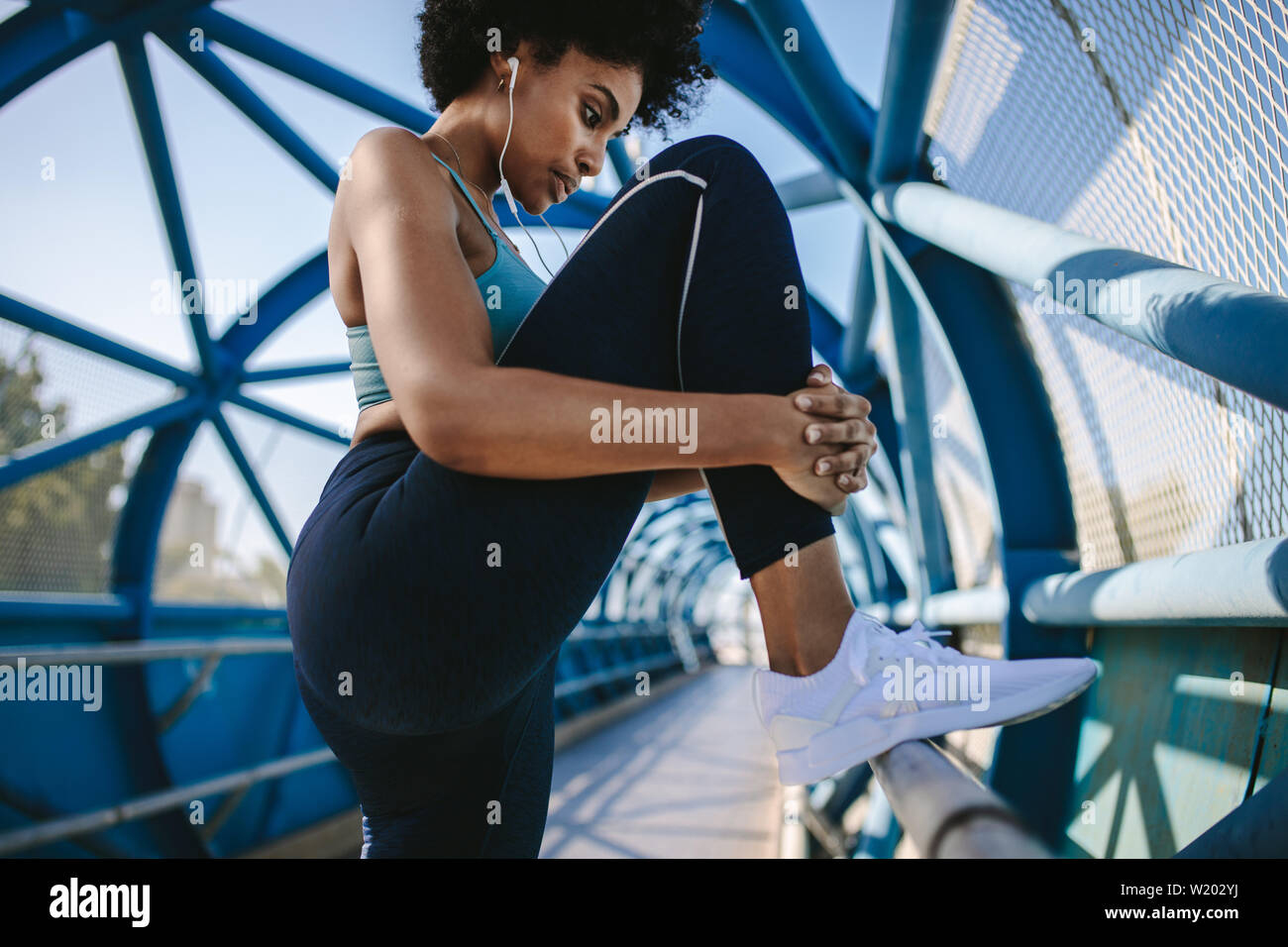 Donna Fitness facendo stretching allenamento delle gambe su un ponte ringhiera. Donna africana facendo allenamento su una passerella Ponte in mattina. Foto Stock