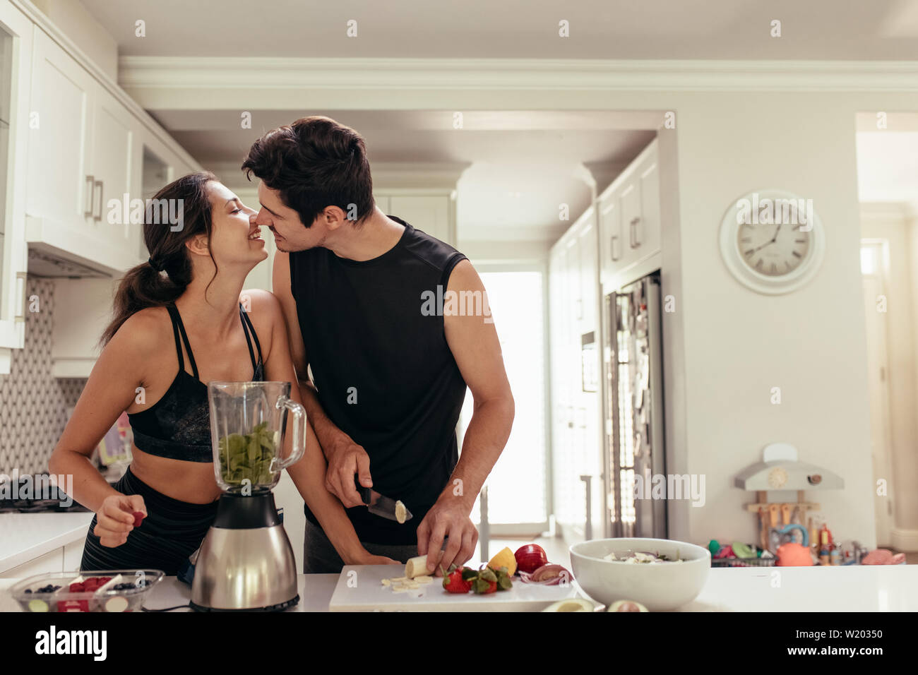 Montare la coppia giovane in amore preparazione frullato sano in cucina. Matura circa a baciare durante la preparazione di una sana prima colazione nella cucina. Foto Stock